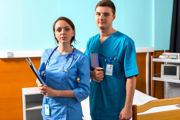 Retrato de médico masculino y femenino en uniforme con fonendoscopio en el cuello sosteniendo portapapeles mientras está de pie en la sala del hospital. Concepto de salud