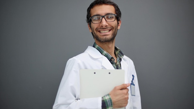 Retrato de un médico masculino positivo posando y sonriendo a la cámara en el fondo gris del estudio