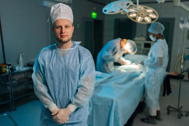 Retrato de un médico masculino en uniformes quirúrgicos de pie posando mirando a la cámara en la oscuridad