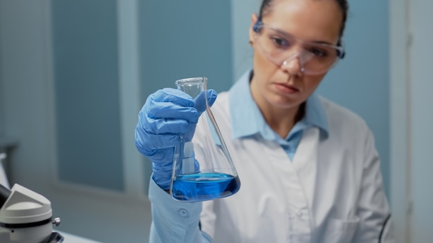 Retrato de médico de microbiología analizando vaso de precipitados químicos