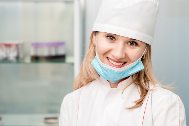 Retrato de médico o enfermera con máscara médica baja sonriendo en el laboratorio.