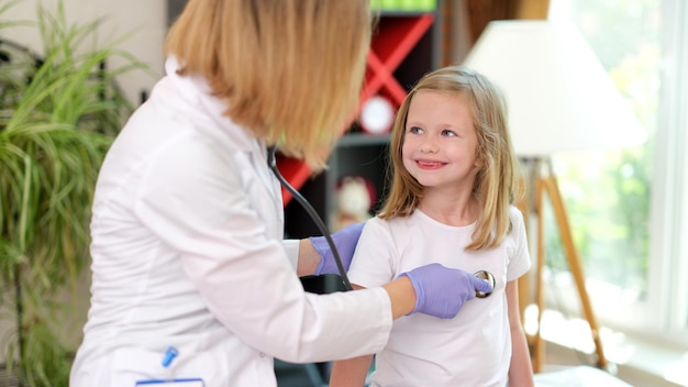 Retrato de médico pediatra examina a niña con estetoscopio pequeño niño sonriente en