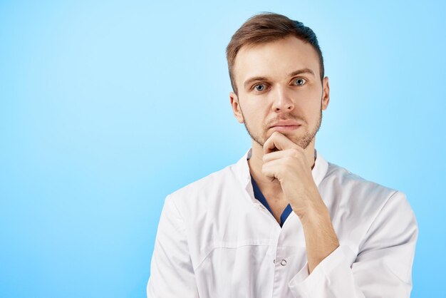 Retrato de un médico pensativo con bata médica blanca y anteojos con expresión facial seria aislada en fondo azul con espacio para copiar