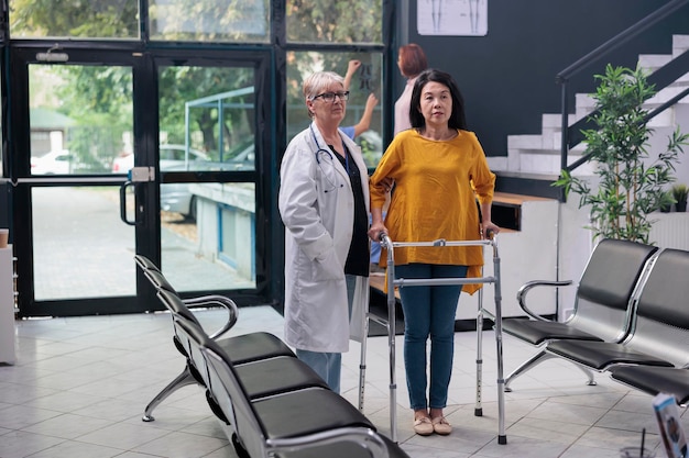 Retrato de un médico que realiza un examen de fisioterapia con un paciente lesionado, apoyando con un marco para caminar para recuperarse después de una lesión por fractura de pierna. Mujer asiática que asiste a consulta de fisioterapia médica.