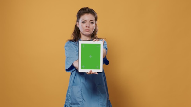 Retrato de un médico que sostiene una tableta y escribe datos médicos que muestran un diseño de maqueta de pantalla verde en la cámara. Médico con uniforme de hospital usando un dispositivo digital de pantalla táctil que presenta espacio de copia.