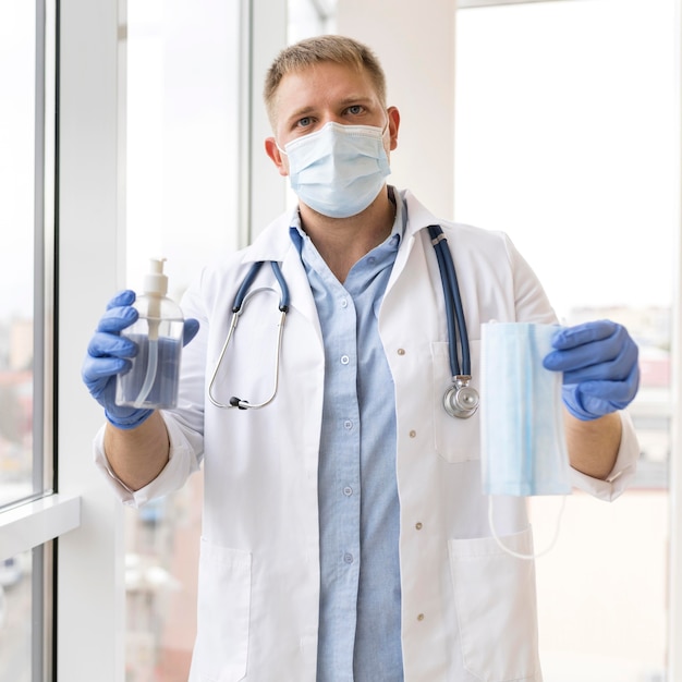 Retrato de un médico sosteniendo una mascarilla y desinfectante de manos