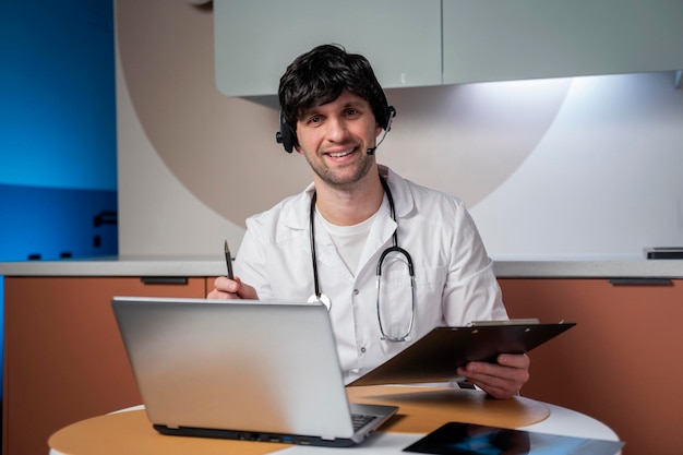 Retrato de un médico en su consultorio usando una computadora portátil para conversar por video con un paciente en línea.