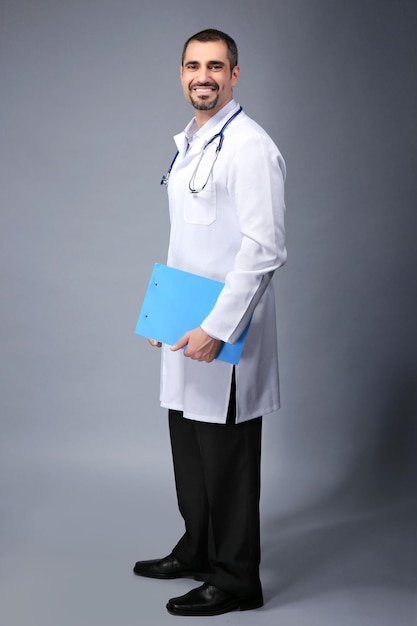 Retrato de un médico con tablero de prescripción en manos sobre fondo gris