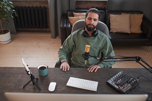 Retrato medio de ángulo alto horizontal de un joven blogger moderno de Oriente Medio sentado en el escritorio viendo