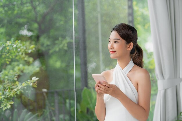 Retrato de medio cuerpo de una chica asiática de pie con un teléfono inteligente mirando la pantalla