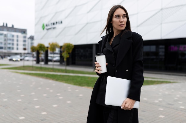 Retrato de medio cuerpo de una elegante mujer de negocios con una computadora portátil y un vaso de café contra el