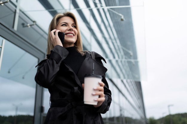 Retrato de medio cuerpo de una empresaria rubia de mediana edad con un teléfono móvil y una taza de café