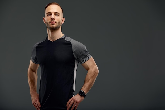 Retrato de medio cuerpo de un joven deportivo con camiseta y pantalones cortos sobre fondo gris de estudio Deportista milenario serio mirando a la cámara Estilo de vida saludable y concepto deportivo