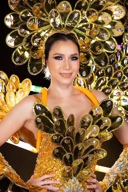 Retrato de medio cuerpo de una mujer asiática transgénero en el carnaval de cabaret, elegante vestido de escamas de pescado dorado, vestido de ala, cabeza sobre fondo oscuro