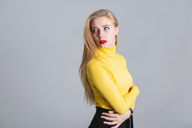 Retrato de medio cuerpo de niña seria en suéter amarillo sobre fondo gris