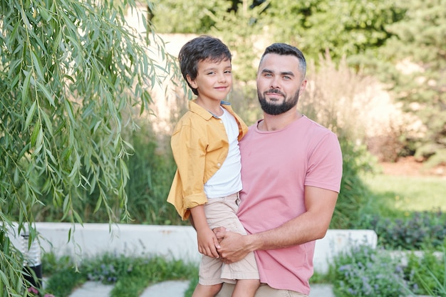 Retrato médio horizontal de um homem barbudo ao ar livre segurando seu filho