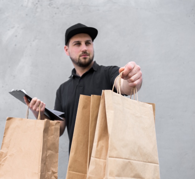 Retrato de mensajería con papeles de pedido y paquetes con comida cerca de la pared gris