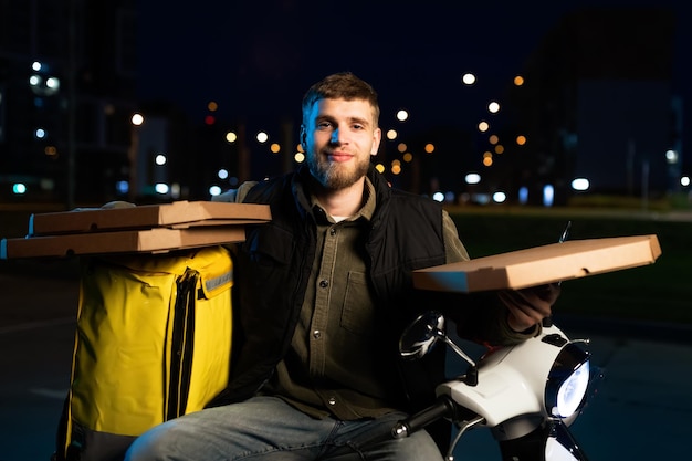 Retrato de un mensajero con cajas de pizza en sus manos Contra el fondo de la ciudad nocturna