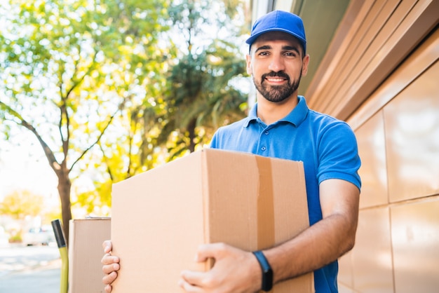 Foto retrato de un mensajero de hombre de entrega con cajas de cartón en las manos al aire libre. concepto de entrega y envío.