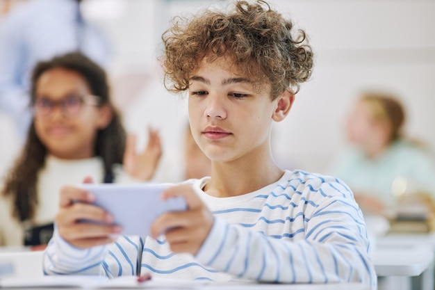 Retrato mínimo de un adolescente sosteniendo un teléfono inteligente y jugando juegos móviles en la escuela