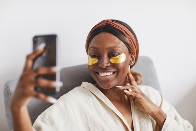 Retrato mínimo de hermosa mujer afroamericana disfrutando de la rutina de cuidado de la piel en casa y hablando por video chat, espacio de copia