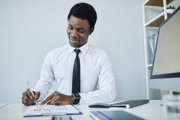 Retrato mínimo de un joven empresario afroamericano en el lugar de trabajo tomando notas