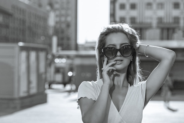 Retrato de moda de adorable joven modelo con gafas caminando por la calle. Espacio vacio. Color monocromático