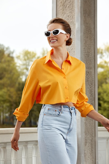 Retrato de moda al aire libre de una elegante mujer de lujo con gafas de sol negras, camisa naranja de moda y jeans Copiar espacio vacío para texto