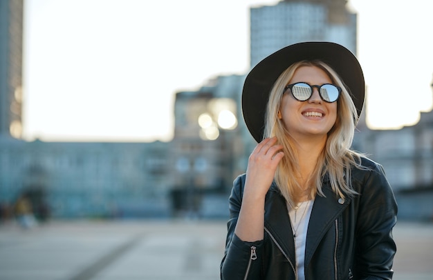 Retrato de moda al aire libre de una feliz mujer rubia con sombrero y gafas de sol de espejo. Espacio para texto