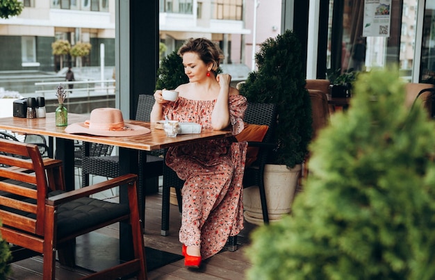 Retrato de moda al aire libre de una mujer impresionante sentada en un café Tomo café y leo un libro viejo una mujer con un vestido y un sombrero