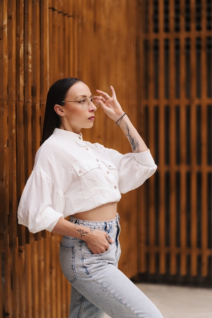 Retrato de moda de una atractiva morena con pelo lacio. mujer vestida con una blusa blanca y gafas posando