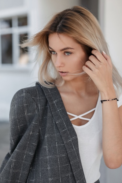 Retrato de moda de una bella mujer joven en una camiseta blanca sin mangas y un abrigo gris en la calle