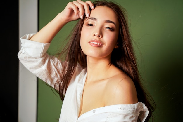 Retrato de la moda de la belleza de la mujer joven asiática sonriente sensual atractiva con el pelo largo oscuro en la camisa blanca