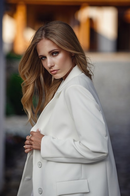 Foto retrato de moda de cuerpo completo al aire libre de mujer de moda en traje blanco posando en la calle de la ciudad del este hermosa foto elegante de una rubia bronceada para una revista de moda