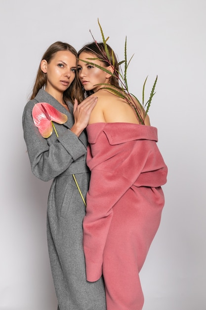 Retrato de moda de dos modelos de mujeres morenas sonrientes en abrigo de verano casual hipster posando sobre fondo gris. Longitud total.