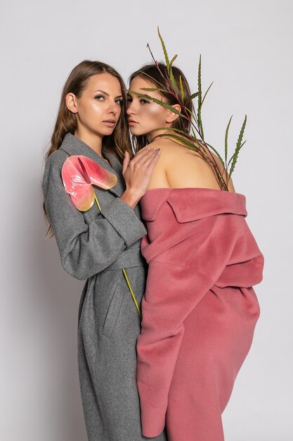 Retrato de moda de dos modelos de mujeres morenas sonrientes en abrigo de verano casual hipster posando sobre fondo gris. Longitud total.