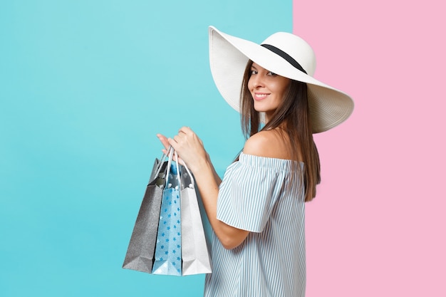 Foto retrato de moda elegante moda hermosa mujer caucásica en vestido de verano, sombrero de sol blanco de ala ancha grande con bolsas de paquetes con compras después de ir de compras aisladas sobre fondo azul pastel.