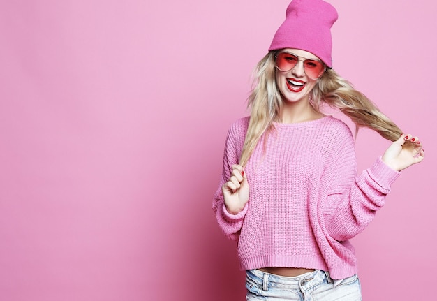 Retrato de moda elegante de mujer joven casual de moda en pulover rosa y sombrero posando sobre fondo rosa