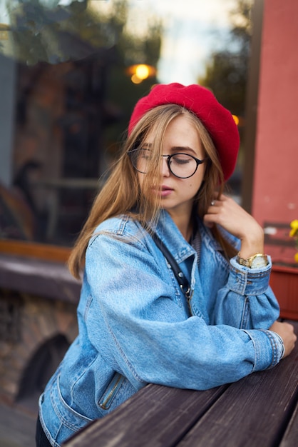 Retrato de moda de estilo de vida soleado de verano de mujer joven inconformista elegante caminando en la calle, vistiendo lindo traje de moda con sombrero rojo