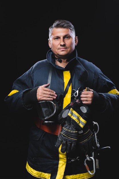 Retrato de moda de un hombre en equipo contra incendios sobre un fondo de estudio negro