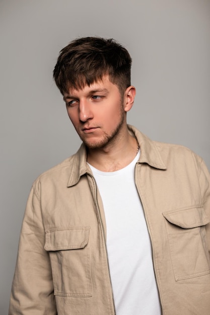 Retrato de moda de un hombre guapo con ropa de moda con una elegante chaqueta marrón y una camiseta blanca de fondo gris