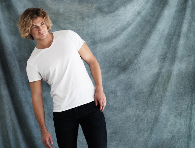 Retrato de moda de hombre joven con camisa blanca plantea en estudio sobre fondo azul.