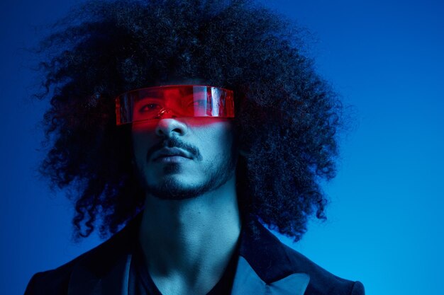 Retrato de moda de un hombre con el pelo rizado en un fondo azul con gafas de sol rojas concepto moderno de moda de color claro multinacional