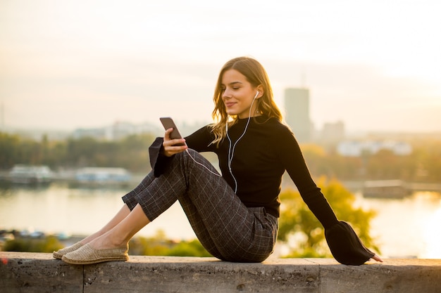 Retrato de moda joven escuchando música desde el teléfono inteligente al aire libre al atardecer