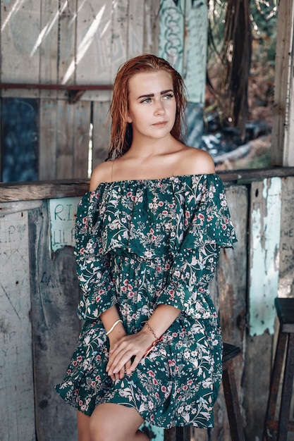 Retrato de moda de una joven modelo con pelo largo jengibre mojado (rojo) en vestido floral verde posando en la cámara. Piel y maquillaje perfectos. Tiro al aire libre