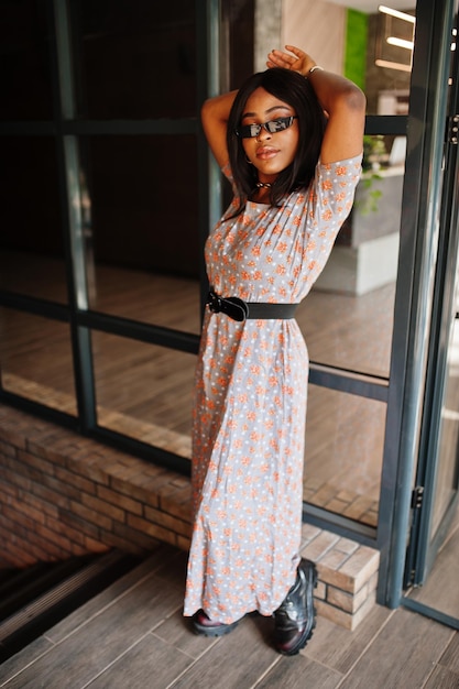 Retrato de moda de mujer afroamericana con vestido largo, botas y gafas de sol en el interior.