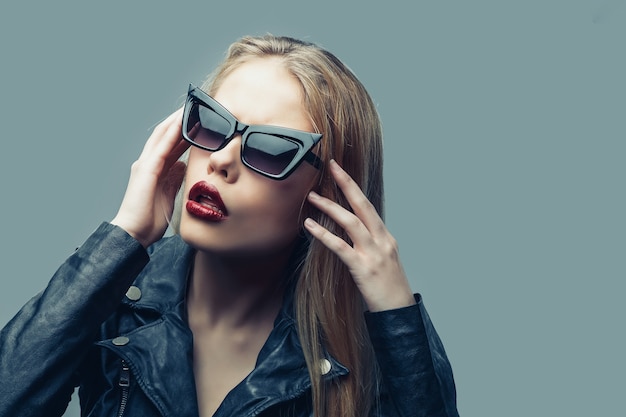 Retrato de moda de mujer con chaqueta de cuero negro, gafas de sol, labios rojos.