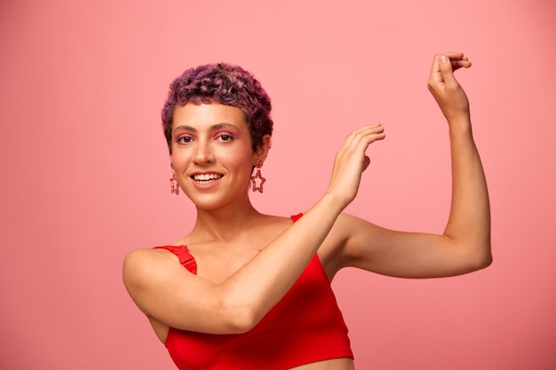 Retrato de moda de una mujer con un corte de pelo corto de color púrpura y una sonrisa con dientes en un top rojo sobre un fondo rosa felicidad