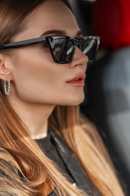 Retrato de moda de una mujer hermosa y elegante con gafas de sol vintage geniales sentada en un auto