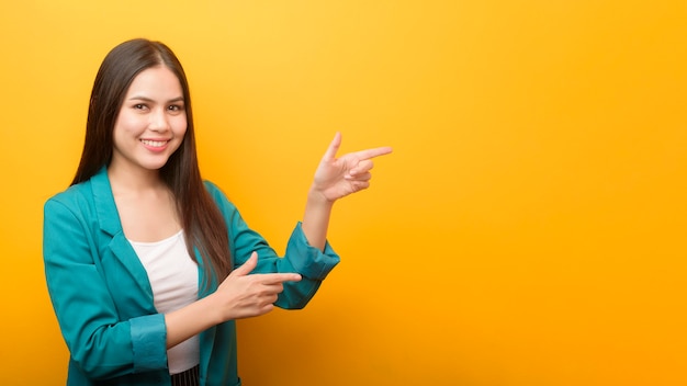 Retrato de moda de mujer hermosa en traje verde mostrando algo en la mano en la pared amarilla